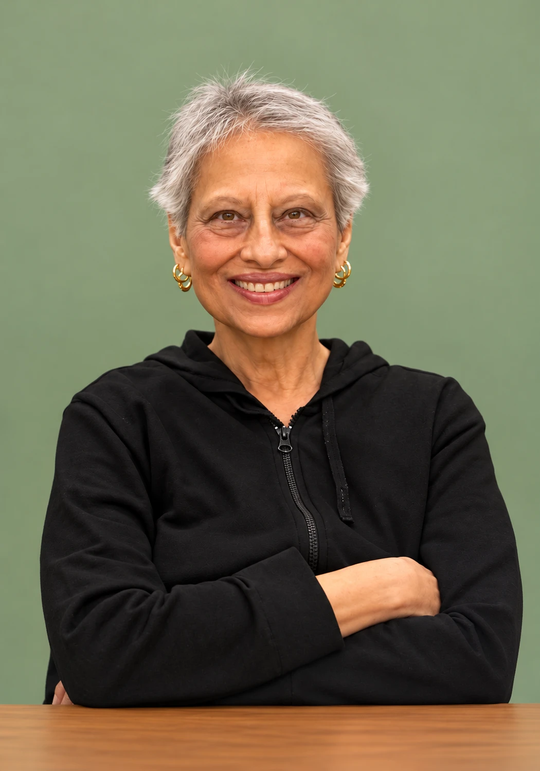 Meenal, smiling, arms folded on a wooden table